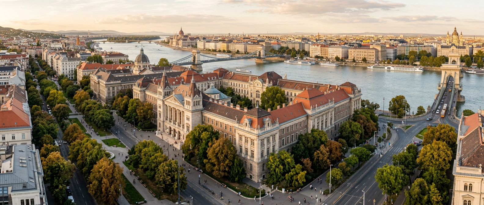 Panoramic view of Budapest University of Economics and Business campus buildings in central Budapest, classical European architecture, tree-lined streets, Danube River visible in the distance, soft afternoon light