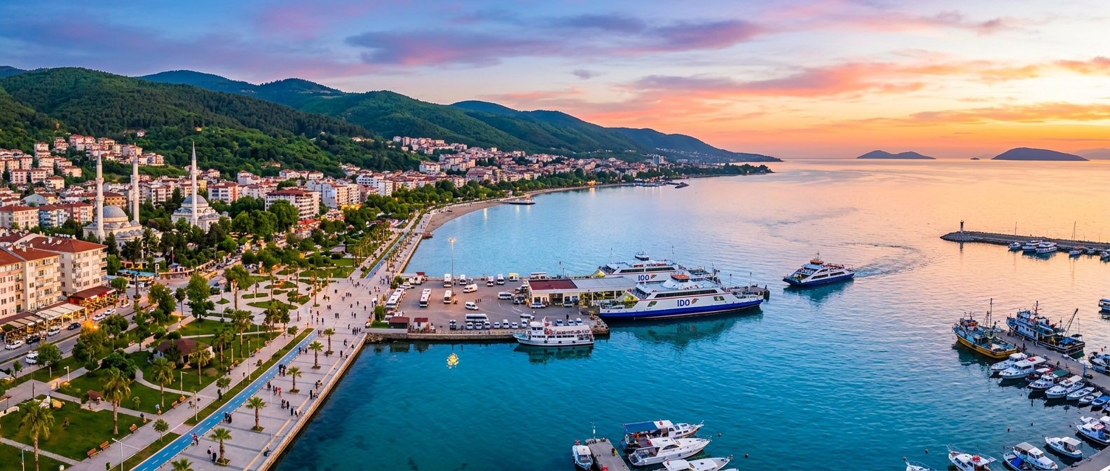Panoramic view of Yalova city coastline along the Sea of Marmara, green hillsides, ferry terminal, coastal promenade, clear blue water, sunset colors