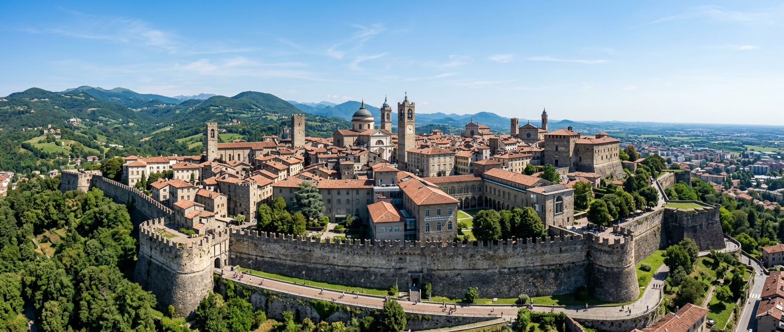 Panoramic view of Bergamo Città Alta with medieval architecture and Venetian walls, university campus buildings nestled among historic stone structures, green hills in the background under a clear Italian sky