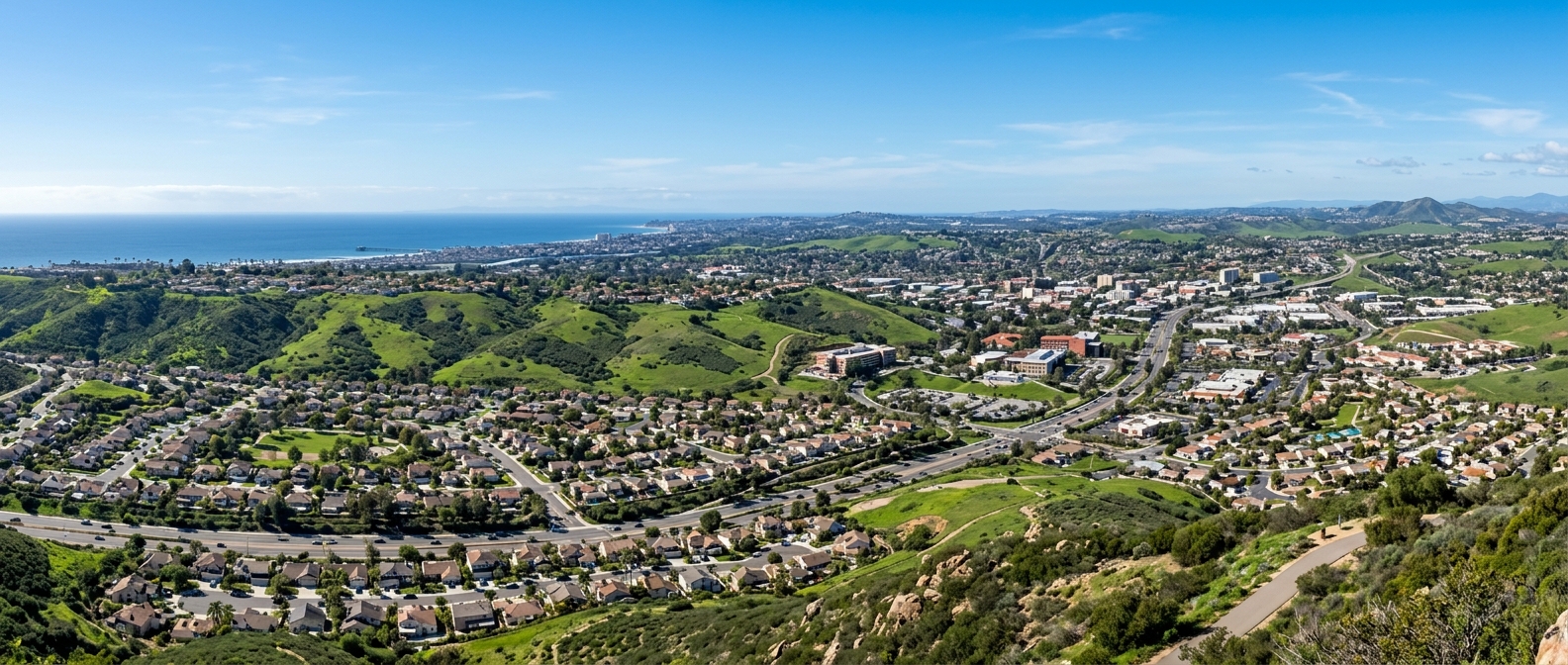 Panoramic view of San Marcos California cityscape with rolling green hills, suburban neighborhoods, and distant views of the Pacific Ocean coastline under clear blue skies